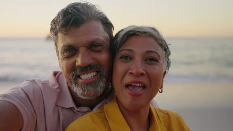 Senior couple smiles for selfie on beach at sunset