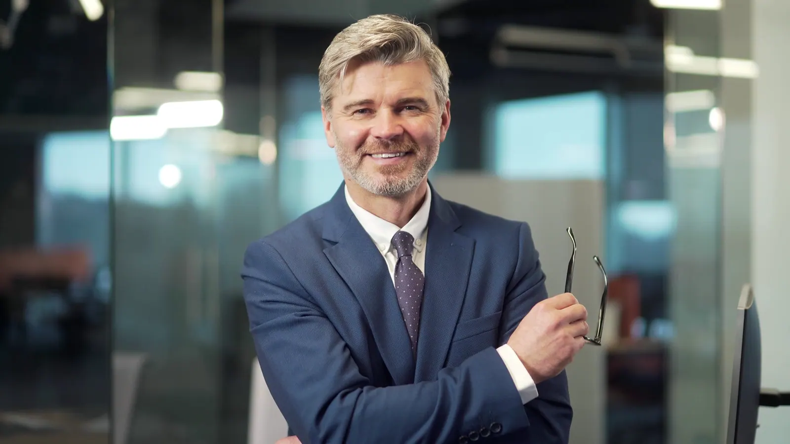 Smiling businessman in suit holding glasses in off