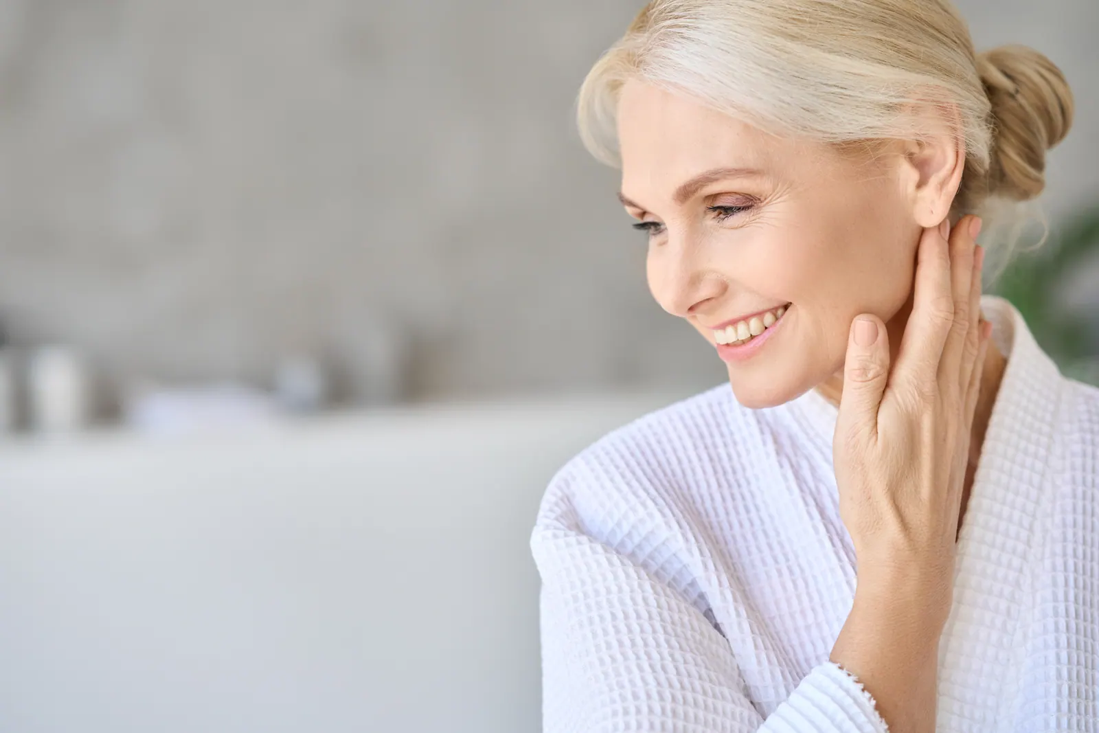Smiling woman in white robe touches her face