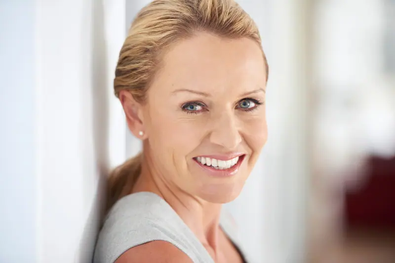 Smiling woman leaning against white wall indoors