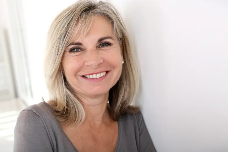 Smiling woman with blonde hair leaning on wall