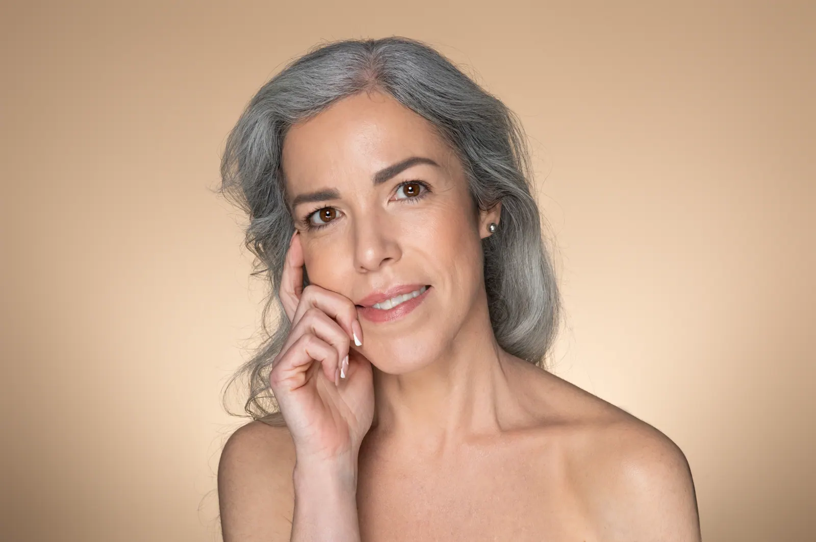 Woman with grey hair posing against beige backgrou